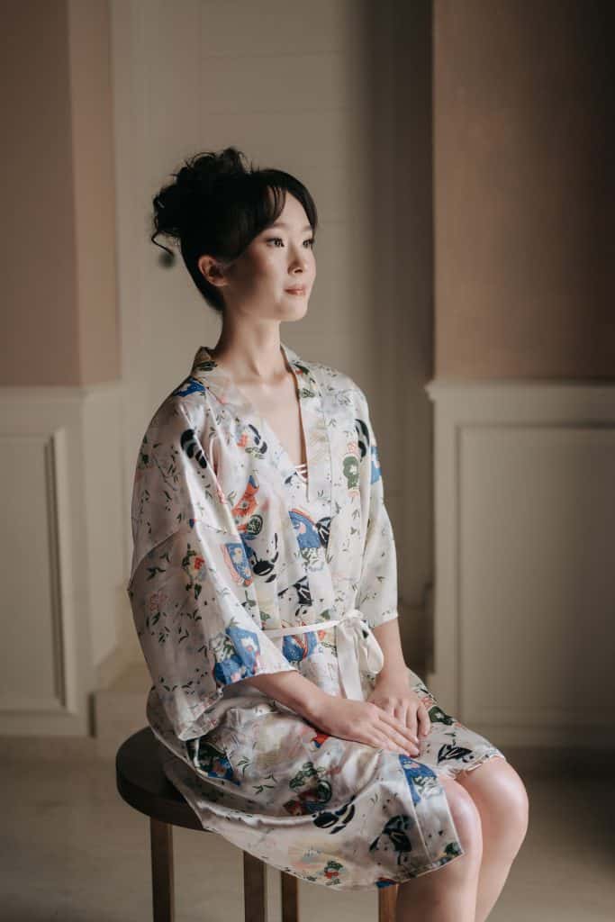 Elegante donna asiatica in kimono floreale seduta su uno sgabello, ambientazione interna raffinata, rappresenta stile e raffinatezza per servizi di wedding planning e eventi di ChiaraB Events.