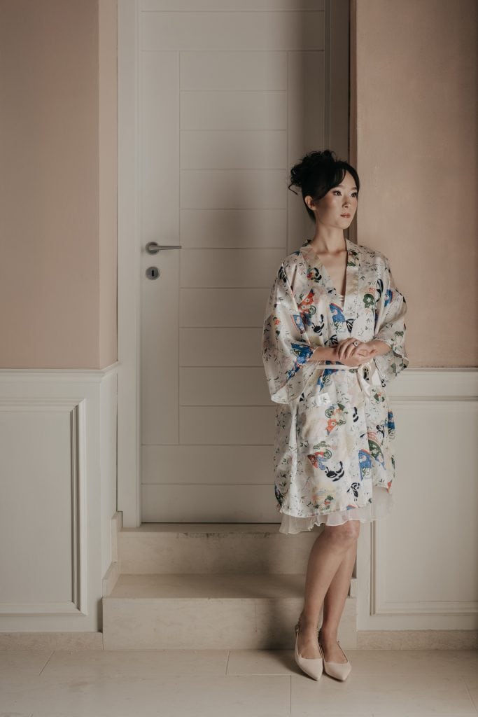 Elegante donna in kimono floreale che si appoggia al muro in un ambiente raffinato, perfetto per servizi di wedding planning e eventi esclusivi.