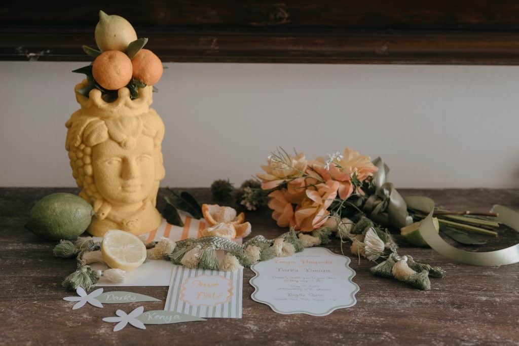 Decorazione di stile boho con testa di Buddha, frutta, fiori e biglietti di auguri su tavolo in legno, perfetta per eventi e matrimoni eleganti.