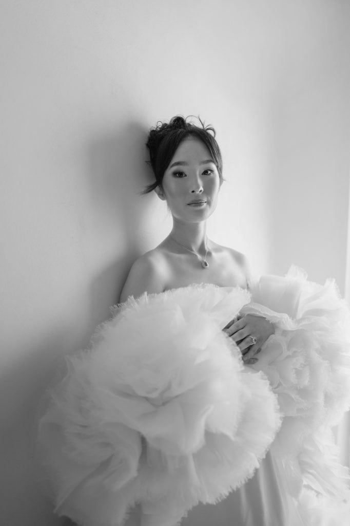 Elegante donna in abito da sposa con dettagli voluminosi, posa in un ambiente neutro, rappresentando un servizio di wedding planning e styling di alta qualità.