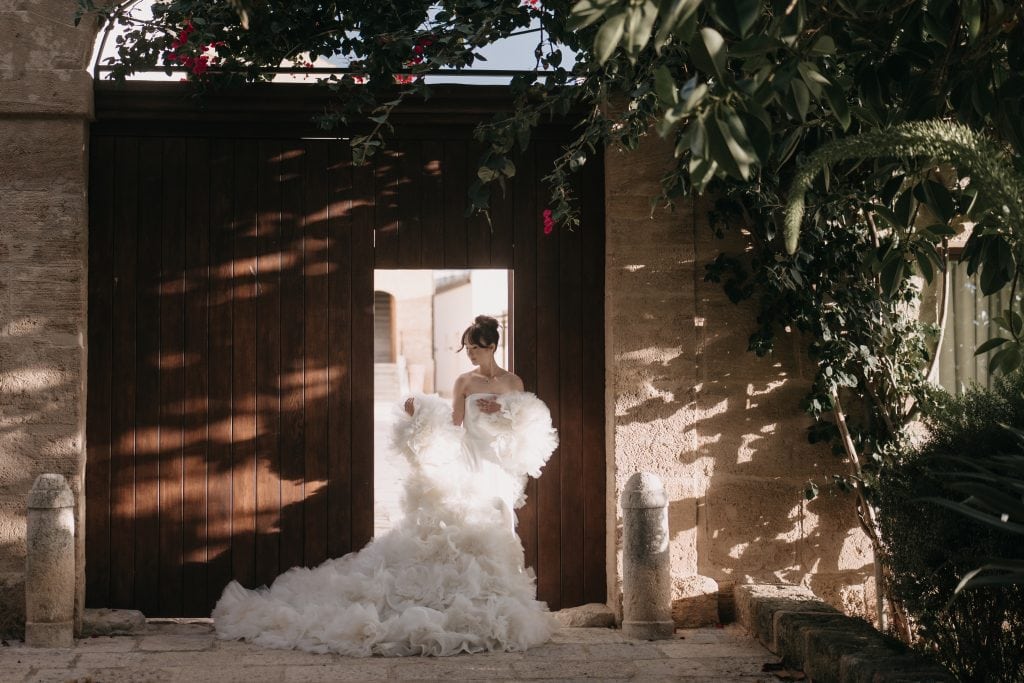 Un'illustrazione di una sposa in abito da matrimonio elegante, che si trova davanti a un grande portone in legno, circondata da vegetazione rigogliosa, pronta per il suo matrimonio, con un'atmosfera r.