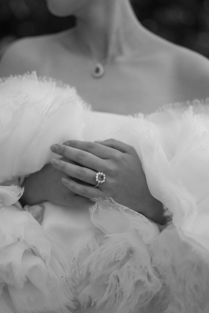 Un anello di diamanti indossato su una mano elegante, con abito da sposa in tessuto leggero e dettagli raffinati, simbolo di eleganza e amore per matrimoni e wedding planning.