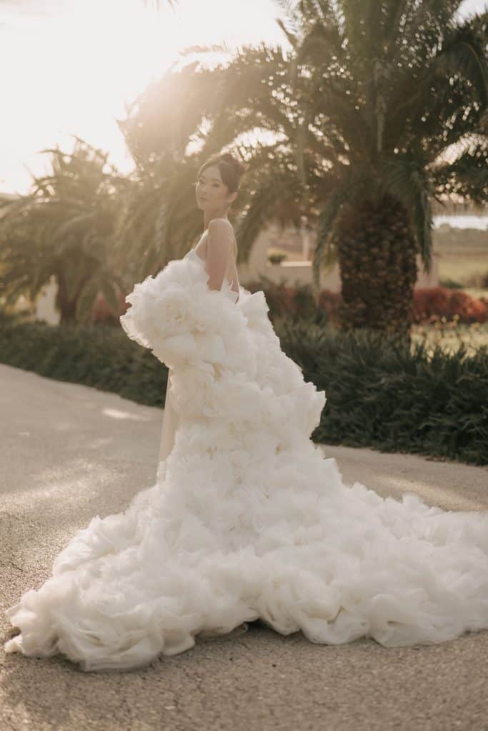 Un abito da sposa elegante con gonna a strati e dettagli in tulle, ambientato in un giardino soleggiato con palme, perfetto per matrimoni romantici e servizi di wedding planning professionale.