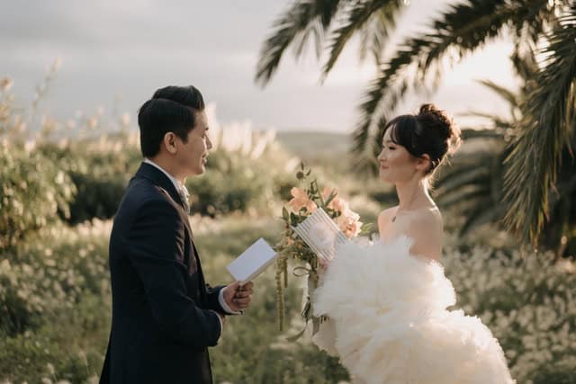 Coppia di sposi in abito da matrimonio con sfondo naturale, durante la cerimonia all'aperto, in un paesaggio con palme e vegetazione, in stile romantico e elegante.