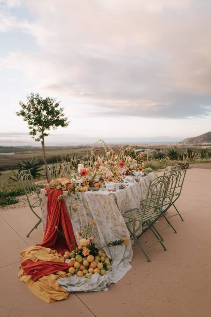 Tavola nuziale all'aperto decorata con fiori, frutta e tessuti eleganti, ideale per matrimoni romantici. Perfetta per un matrimonio all'aperto con vista panoramica, curata da ChiaraB Events.