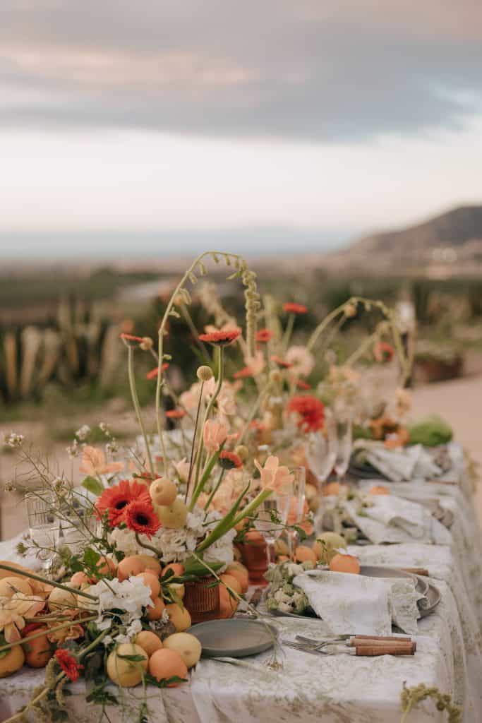 Luci di candela e decorazioni floreali eleganti su un tavolo da matrimonio all'aperto con vista mare al tramonto.