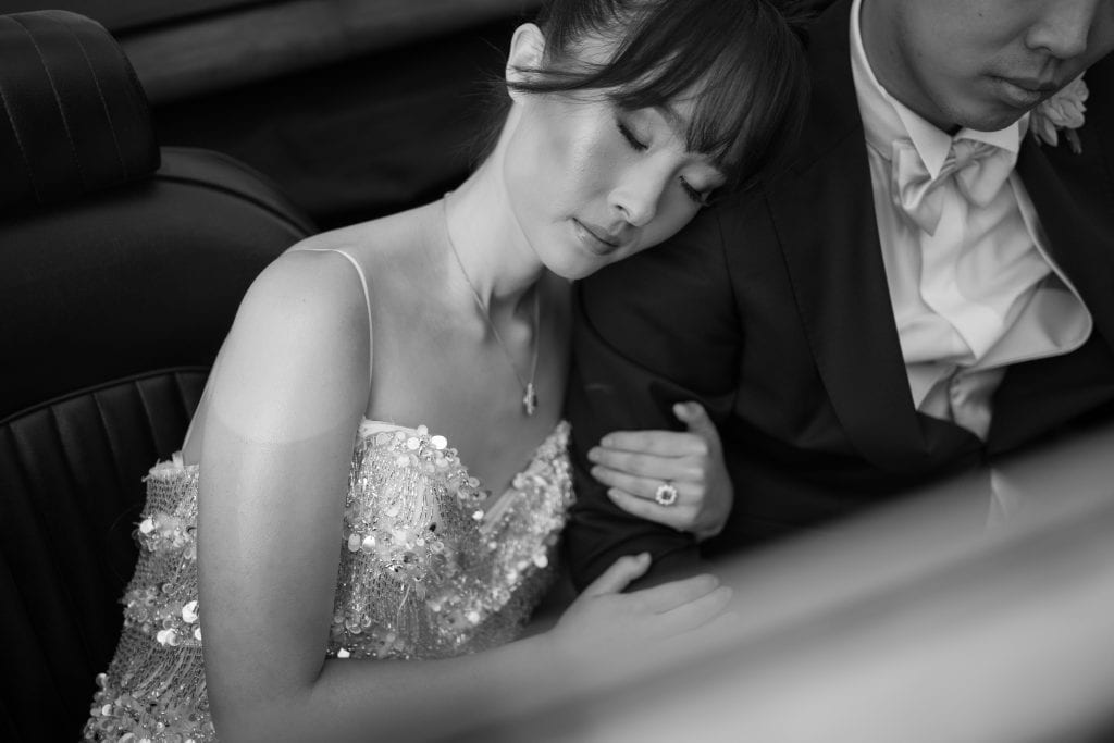Elegante coppia di sposi seduti in auto, momento intimo e romantico durante il matrimonio, con abiti da cerimonia raffinati e atmosfera emozionante.