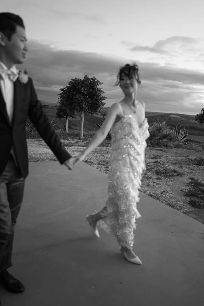 Un matrimonio elegante con sposi che si tengono per mano all'aperto, in un paesaggio rurale al tramonto, perfetto per servizi di wedding planning e organizzazione matrimoni.