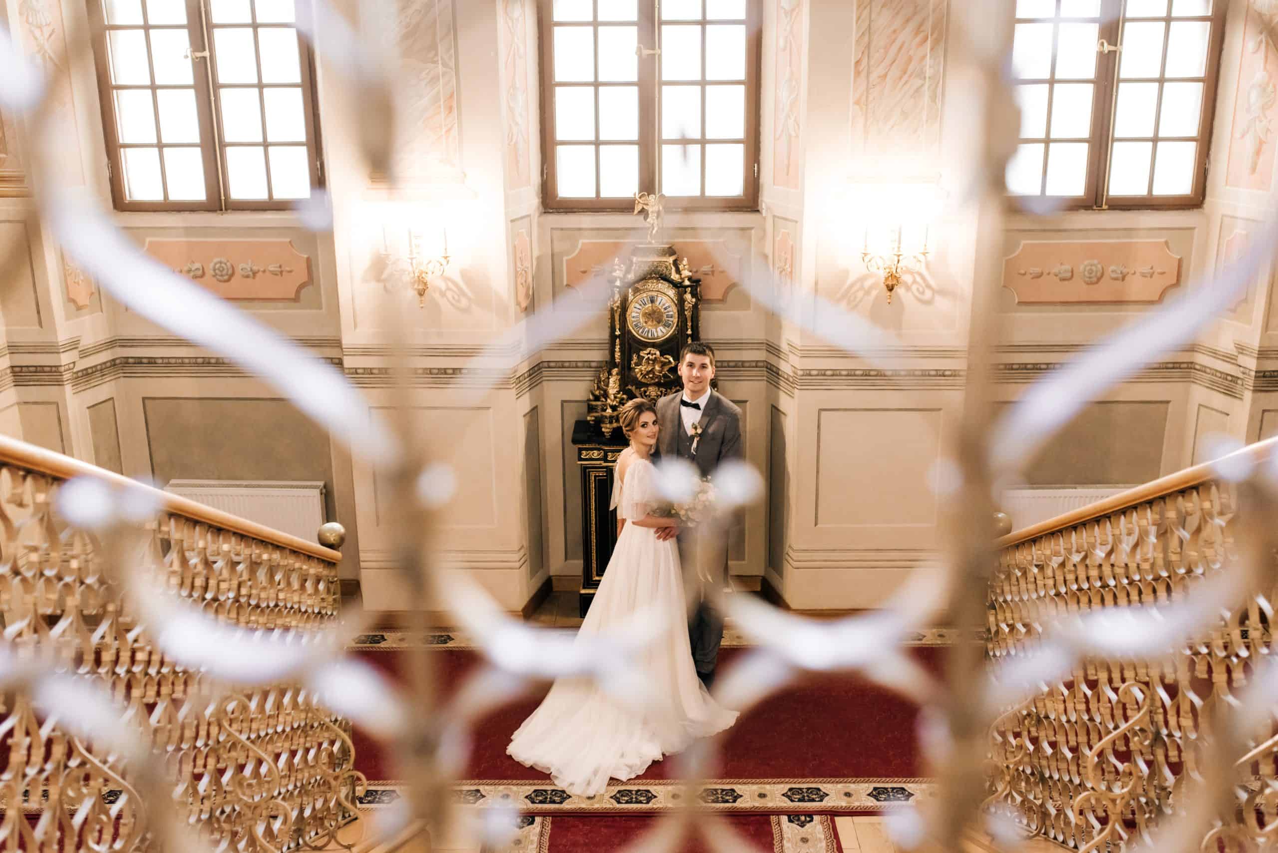 एक भव्य ऐतिहासिक हॉल में सुरुचिपूर्ण विवाह, जिसमें समारोह के कपड़े पहने वर-वधू, परिष्कृत सजावट और रोमांटिक माहौल है, उच्च गुणवत्ता वाली वेडिंग प्लानिंग सेवाओं के लिए उपयुक्त।