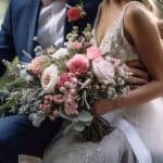 Un matrimonio elegante con sposa che tiene un grande bouquet di fiori rosa e bianco, seduta accanto allo sposo in un ambiente naturale e romantico.