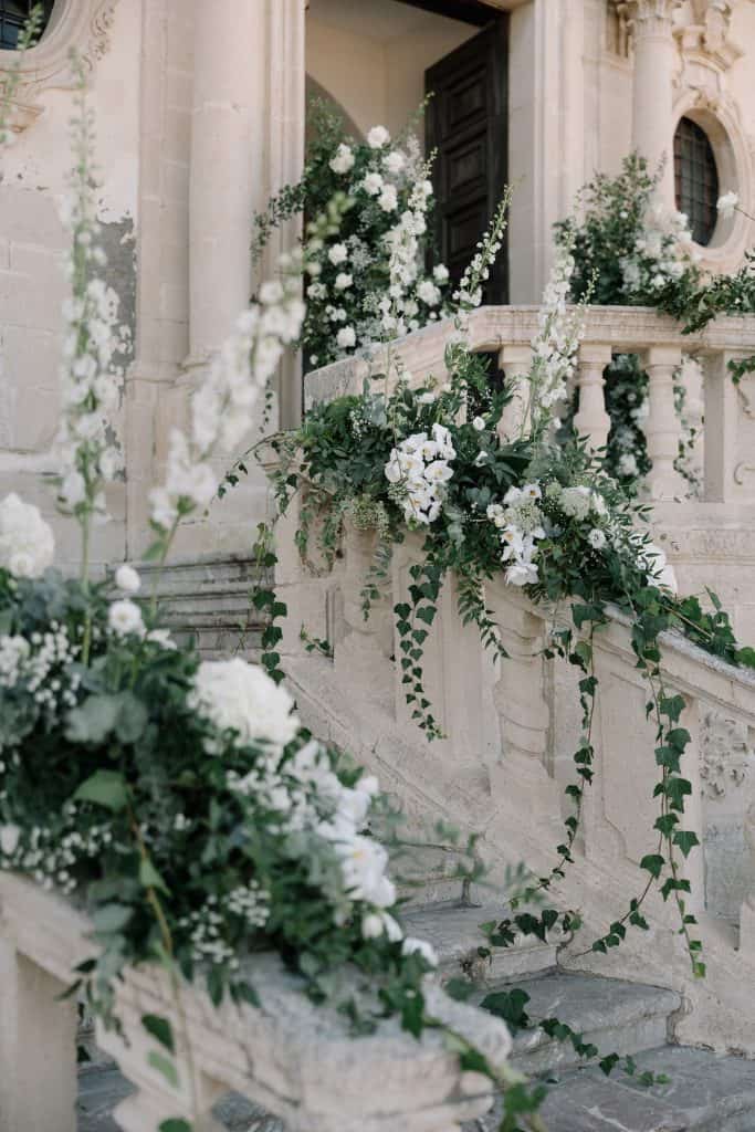 Decorazioni floreali bianche e verdi su scale e balaustre di un edificio storico.