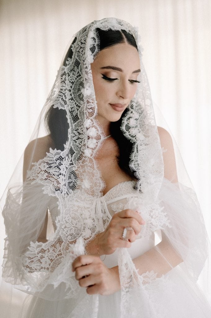Sposa con velo di pizzo raffinato, pronta per il matrimonio, in un ambiente luminoso. Perfetta per servizi di wedding planning e matrimoni eleganti.