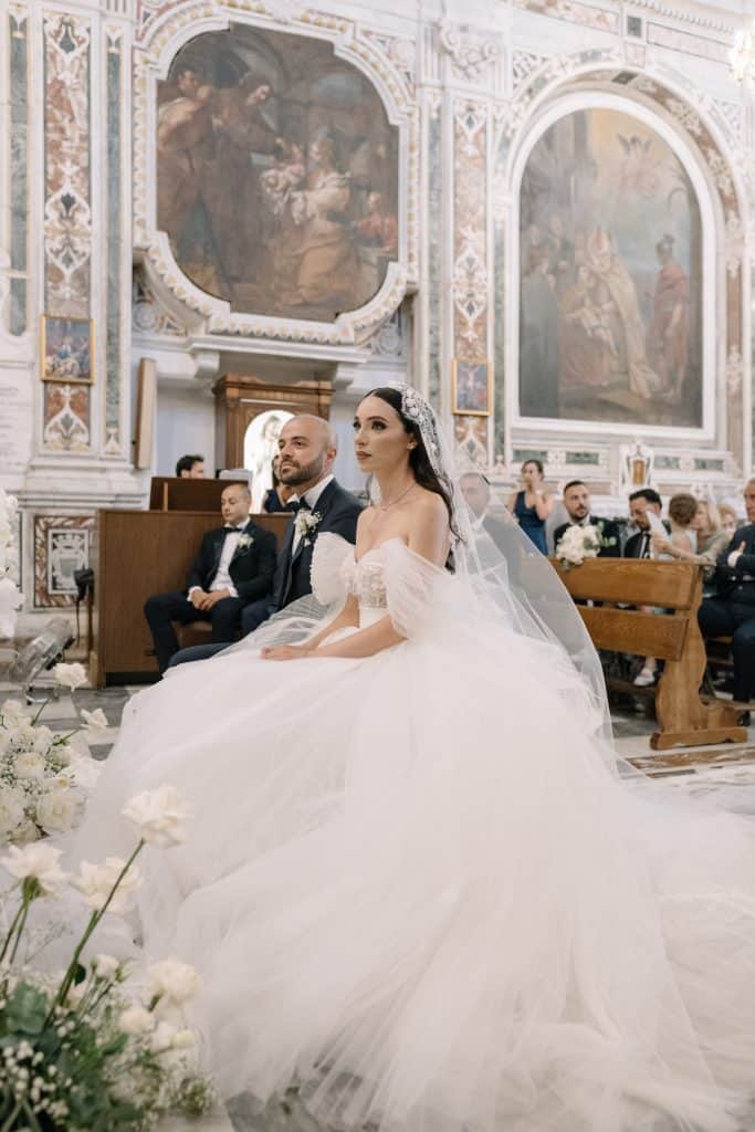 Sposi Alberto e Valeria durante il matrimonio, in una chiesa storica con decorazioni barocche e affreschi antichi, catturando un momento di intimità e gioia.