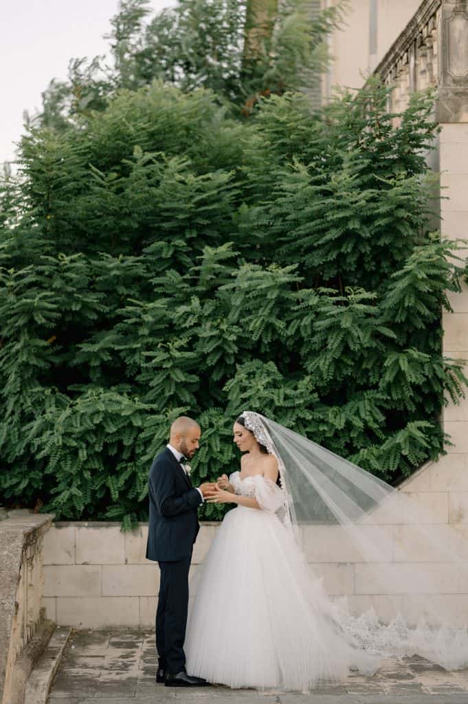 Coppia di sposi in abito da matrimonio e abito da sera, scambiandosi un momento speciale all'aperto, con grande albero verde sullo sfondo, durante il matrimonio di Alberto e Valeria.