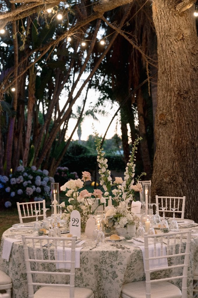 Tavolo da matrimonio all'aperto decorato con fiori bianchi e candele, immerso in un'atmosfera romantica sotto gli alberi, perfetto per un matrimonio indimenticabile.