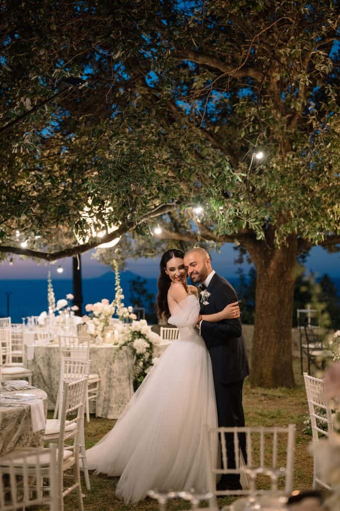 Alberto e Valeria durante il loro matrimonio all'aperto, circondati da luci soffuse e decorazioni floreali, in un'atmosfera romantica e raffinata.