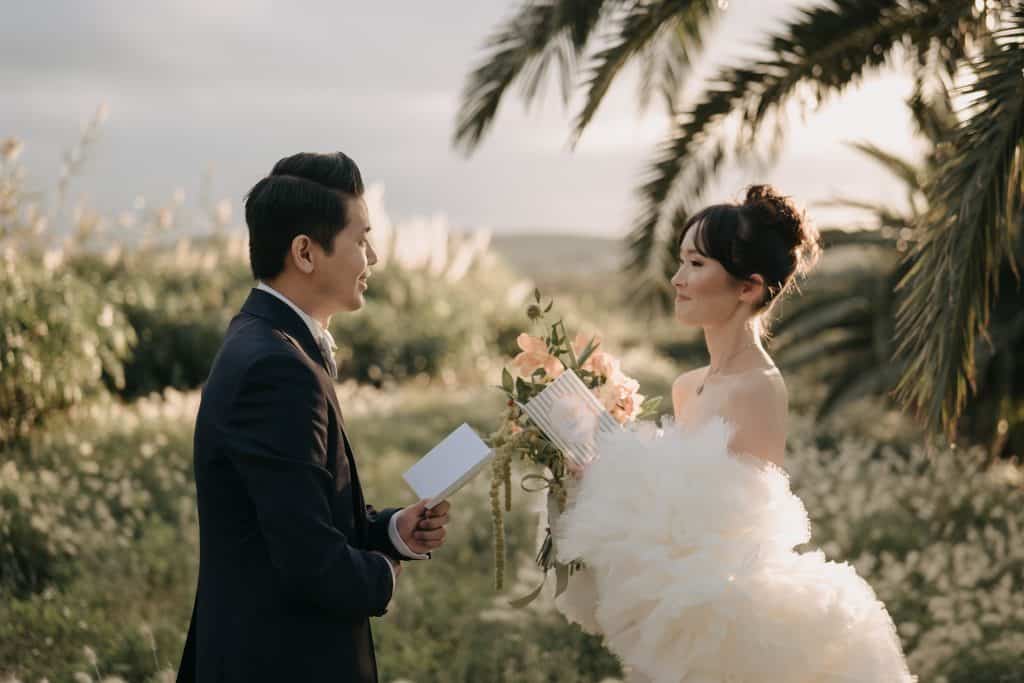 Matrimonio romantico all'aperto con sposi che si scambiano promesse, circondati da natura e palme, perfetto per servizi di wedding planning e organizzazione eventi.